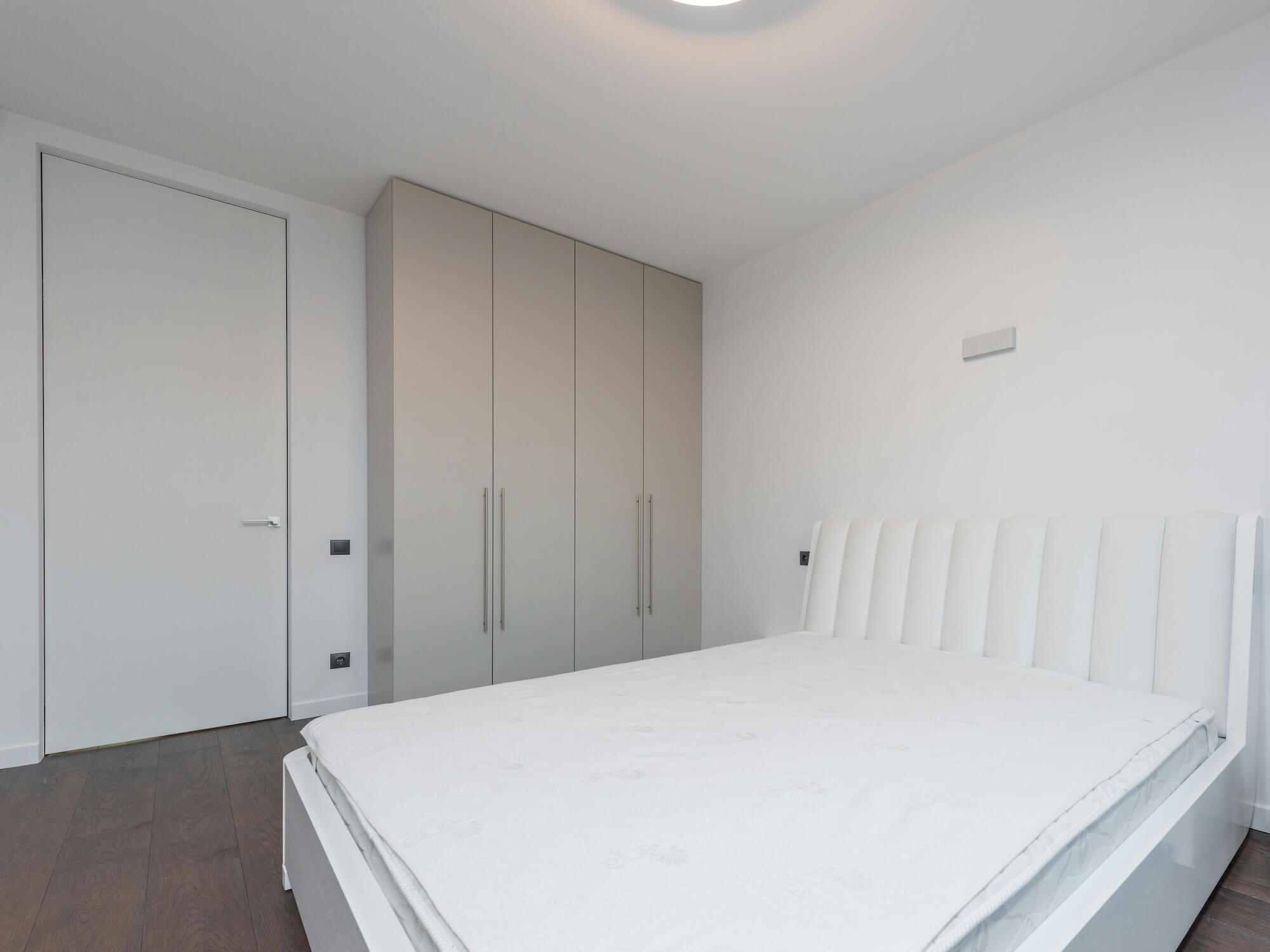 Kleiderschrank mit Schranktüren in grau hinter einem weißen Bett